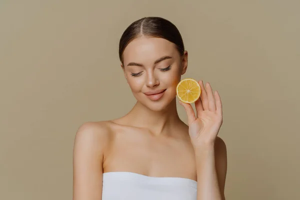 美しいブルネットの若い女性の肖像を濃縮ダウンホールド新鮮なレモンスライスは 天然の美しさ製品をお勧めしますバスタオルで包まれた自然な有機顔の治療を好む屋内ポーズ — ストック写真