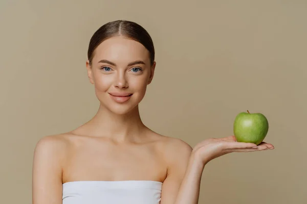 バスタオルに包まれた天然化粧台の美しい女性の写真は 茶色の背景に隔離された食事のための製品をお勧めします緑のリンゴを保持しています自然な自家製顔のマスクを作ります — ストック写真