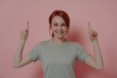 Mutlu beyaz kadın işaret parmaklarıyla yukarıya doğru işaret ediyor ve pembe arka planda izole edilmiş reklam ürününü tanıtırken neşeyle gülümsüyor. Reklam kavramı