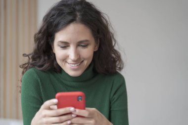 Cep telefonu kullanan, ofis masasında oturan, kendine güvenen İspanyol iş kadını, genç bayan serbest çalışan ya da özel öğretmen, olumlu bir gülümsemeyle telefon ekranına bakıyor, işten uzaklaştırılmış, internette sohbet ediyor.