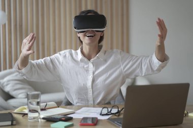 Heyecanlı Avrupalı iş kadını iş yerinde VR gözlüklerini test ediyor, iş yerinde dizüstü bilgisayarla oturuyor ve yaratıcı sanal gerçeklik teknolojisi kullanıyor, tatilde 3 boyutlu oyun oynayan kadın işçi