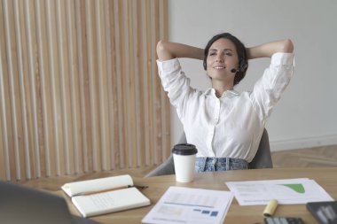 Kablosuz kulaklıklı, rahat bir pozisyonda oturan, yan bakan, müşteri aramaları arasında mola veren, uzaktan çevrimiçi çalışan meditasyon yapan kadın girişimci.