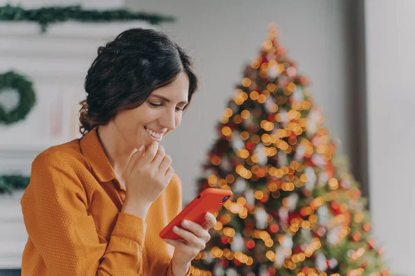 Χαρούμενη Ισπανίδα Κυρία Κάθεται Στο Σαλόνι Διακοσμημένη Χριστουγεννιάτικο Δέντρο Κοιτάζοντας — Φωτογραφία Αρχείου