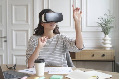 İş için VR uygulaması. Sanal gerçeklik kulaklığı takan genç bir kadın 360 derece içeriği seyrediyor, iş yerinde otururken taklit ortama daldırılıyor, 3D gözlüklü kadın çalışan.