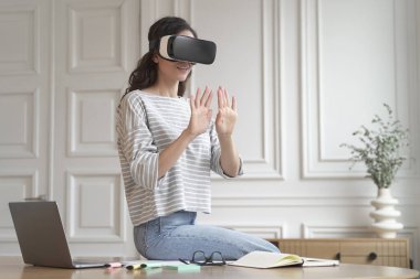 Sanal gerçeklikteki dijital arayüzle etkileşim halinde olan genç ve heyecanlı kadın serbest çalışan VR gözlük takıyor, elleri havada üç boyutlu oyunda görünmez duvara yaslanmış gibi görünüyor.