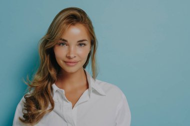 Beyaz tişörtlü, boyalı sarı saçlı, hoş bir gülümseme takınan beyaz saçlı beyaz bir kadın mankenin portresi. Açık mavi stüdyo duvarına izole edilmiş ve reklam için yer ayırtılmış.