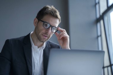 Resmi takım elbiseli ve gözlüklü konsantre genç Alman işadamı dizüstü bilgisayara bakıyor, ofiste çalışırken internette dalgın erkek sörf bilgisi. İş kavramındaki iş adamları