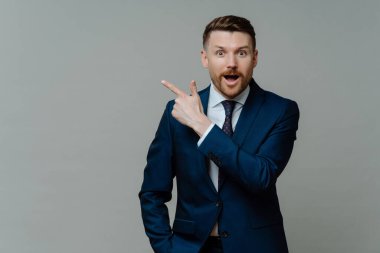 Surprised elegant businessman empoyee advertises copy space dressed in formal outfit isolated over grey studio background. Successful entrepreneur promots your product or service. Best choice