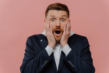Young shocked happy red haired guy in casual wear staring with surprise at camera, getting some incredible news, guy dropping jaw from amazement while posing against pastel pink background