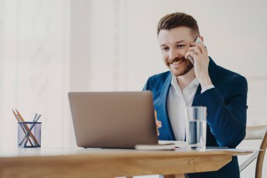 Resmi takım elbiseli genç çekici iş adamı telefonda konuşurken gülümsüyor ve dizüstü bilgisayara bakıp gördüklerini onaylıyor. Yönetim kurulu başkanı, şık bir iş yeri ve minimalist ofis ortamında oturuyor.