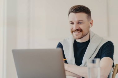 Başarılı erkek serbest çalışan iş arkadaşlarıyla internet konferansında kulaklık ve dizüstü bilgisayar kullanıyor, iyi haberler duymaktan mutlu oluyor, ofiste günlük kıyafetlerle konuşan neşeli iş adamı.