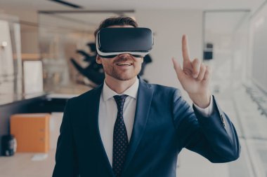 Sanal iş görüşmesinde VR gözlüklü genç başarılı işadamı parmaklarıyla havaya dokunuyor. Üç boyutlu gözlüklü adam ofisinde çalışırken artırılmış gerçeklikte konferansa katılıyor.