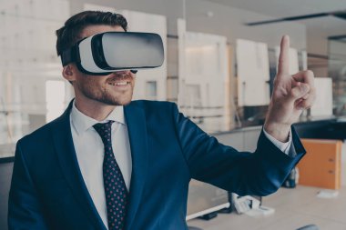 VR gözlük takan, 360 derecelik kulaklık kullanıcı arayüzü ile etkileşimde bulunan genç finansör, ofisinde dururken, 3D menüdeki içeriği seçer.