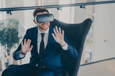 Genç işadamı VR kulaklık takıyor. Şirket finans merkezi lobisinde oturan ofis çalışanı veya CEO 'su, sanal gerçeklik yoluyla iş projelerini yönetmek için yeni yenilikçi metodu test ediyor.