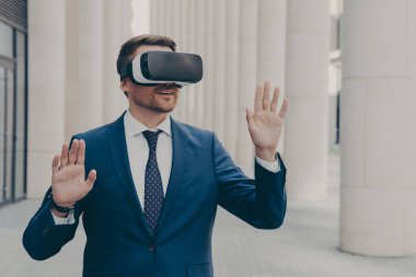 Yeni siber uzay deneyimi. Şaşırmış erkek ofis çalışanı resmi olarak üç boyutlu gözlüklerle dışarıda duruyor ve sanal arayüzle etkileşime geçiyor, sanal nesnelere dokunuyor, iki elini de havada hareket ettiriyor.