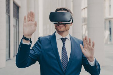 Mavi takım elbiseli bir işadamı mobil VR kulaklık kullanarak sanal gerçekliği deneyip tecrübe etmeye çalışıyor. Bunu reklam ve gelecek projeleri için kullanmayı planlıyor. Aydınlanmış binanın önünde tek başına duruyor.