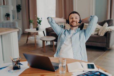 Uzaktan kumandalı işini yaparken mikrofon ve dizüstü bilgisayarla rahat ofisinde oturup el ele tutuşan mutlu bir erkek serbest yazar. Serbest ve uzak çalışma konsepti