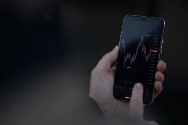 Yatırımları yöneten tüccarların ve mobil uygulamalardaki hisse senedi alım satımlarının kırpılmış görüntüsü. Finansal grafik grafikli akıllı telefon ekranına erkek eli değmiş. Borsa ve çevrimiçi ticaret kavramı