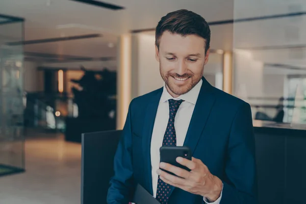 사업가 사무실 복도에 스마트폰을 미소짓고 동료들로부터 스마트폰을 읽으면서 — 스톡 사진