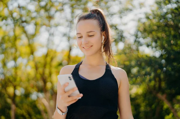 Outdoor Shot Pleased Sporty Woman Focused Smartphone Checks How Many — Stock fotografie
