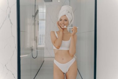 Dişlerini fırçalarken banyoda duran, beyaz klasik iç çamaşırlı, fit vücutlu genç bir manken. Kişisel vücut bakımı ve ağız temizliği kavramı