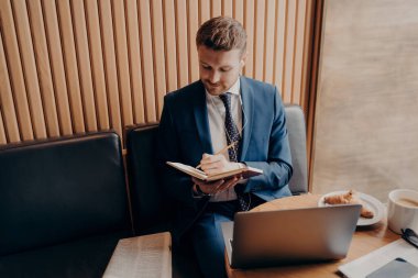 Resmi olarak sakallı genç işadamı kafede oturup not defterine notlar yazarken aynı zamanda dizüstü bilgisayardaki eğitim seminerlerini dinliyor ve kahvaltıda uzaktan çalışıyor.