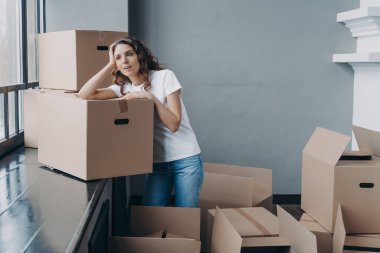 Girl is dreaming while sitting on floor in new apartment. Young woman enjoying view looking at the window. Happy attractive hispanic woman unpacking boxes. Concept of future and perspective.