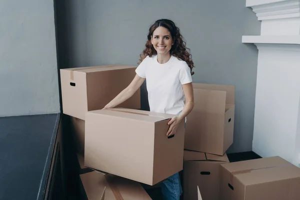 Happy woman is carrying box and smiling. Lady is purchasing real estate and unpacking cardboard boxes in new apartment. Young woman is going to rent house. Changes and new life concept.