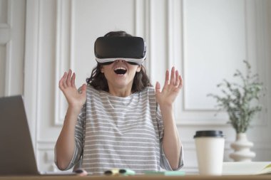 Heyecanlı, neşeli girişimci kadın sanal gerçeklik teknolojisini test ediyor. Sanal gerçeklik gözlüğü takıyor. Ana ofiste oturuyor, 360 derecelik kulaklıkla etkileşimde.