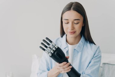 Young girl with disability puts together her bionic prosthetic arm, adjusting the position and grip of myoelectric prosthesis. Pretty modern woman using artificial limb. Disabled people