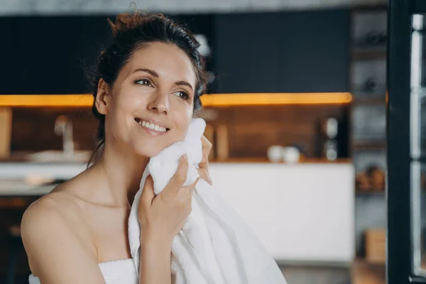 Happy young latina girl wiping face with cotton towel after morning washing, enjoying delicate touch. Smiling female drying her glowing healthy skin after shower. Skincare treatment, self-care concept