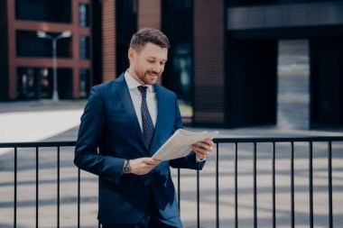 Modayı takip eden takım elbiseli iş adamı finans şirketlerinin şirket birleşmesiyle ilgili haberleri okuyor. Ofis merkezinde yürüyen, resmi kıyafet kontrolü yapan bir erkek dergi hakkında makale yazıyor.