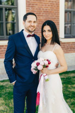 Sadece evli çift birbirinize sarılın, mutlu ifadeler varsa, birbirine yakın durmak. Güzel esmer erkek beyaz gelinlik, siyah takım elbiseli bouquete ve onun yakışıklı damat tutar