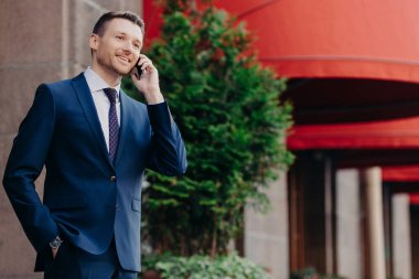 Resmi takım elbiseli, akıllı erkek yöneticinin yan fotoğrafları, akıllı telefon aracılığıyla telefon görüşmesi, el ele tutuşmalar, iletişim tarifelerinin keyfini çıkarmalar, şehir bölgesinde açık havada durmalar.