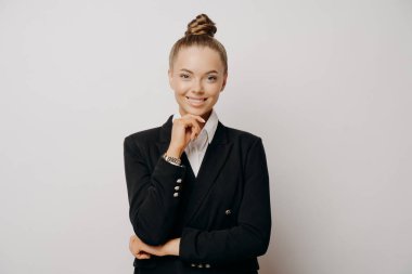 Neşeli kadın ofis çalışanı portresi, günlük giysiler içinde, kendine güvenen vücut dili çenesinde, iş kadını kendini mutlu ve çalışmaya hazır hissediyor, ışık duvarına karşı ileriye bakıyor.