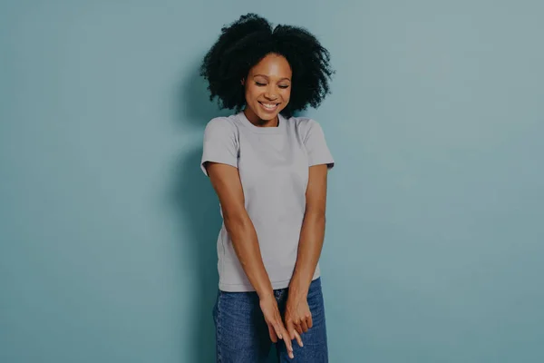 Cute young african lady wearing casual outfit looking down with with shy timid face expression, shrugging shoulders and feeling embarrassed with uncomfortable question, isolated over blue background