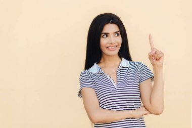 Sevindim hoş gülümseme ile esmer kadın, uzun siyah saçlı, ile gösterir ön parmak yukarıya doğru reklam veya promosyon arka plan için boş alan gösterir. İnsanlar, reklam kavramı