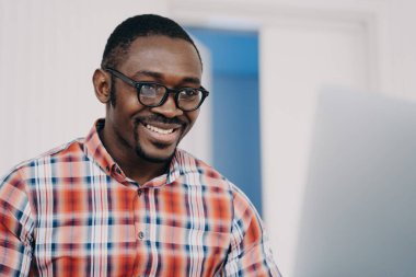 Gözlüklü Afrikalı Amerikalı bir menajer online projede çalışıyor, dizüstü bilgisayara bakıyor, gülümsüyor. Gözlüklü mutlu zenci ofis çalışanı işlerle e-posta okuyor. Bilgisayarda iyi haberler..