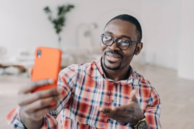 Gülümseyen Afro-Amerikan adam, elinde gözlüklerle modern uygulamalar kullanarak video görüşmeleri yapıyor. Sosyal ağlarda iletişim kuran, akıllı telefon ekranına bakan dost canlısı genç siyahi adam..