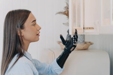 Engelli kız elektronik siber elle dolabı açıyor. Evde yapay kollu genç Avrupalı bir kadın var. Modern biyonik protezin işlevleri. Engelli kişi kavramının rutini.