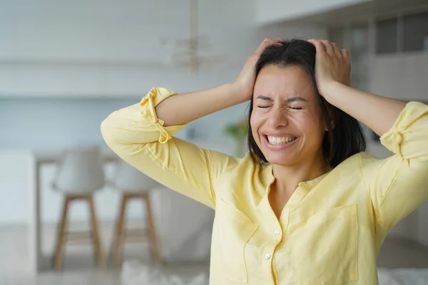 Stressed woman holding head with closed eyes, getting angry, nervous, standing at home. Annoyed female suffering from headache, loud music, noisy neighbors. Premenstrual syndrome, burnout concept.