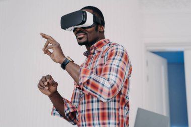 VR gözlük takan Afrikalı bir adam sanal objelere parmaklarıyla dokunuyor, siber uzayla etkileşime geçiyor. Sanal gerçeklik gözlüklü modern siyahi adam online video oyunu oynuyor. Yüksek teknoloji konsepti.