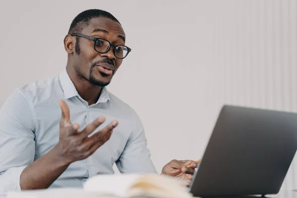 非裔美国商人在笔记本电脑上通过视频电话与同事讨论工作项目 迷惑的黑人男性商人 在网上用计算机交谈 给办公室打手势 — 图库照片