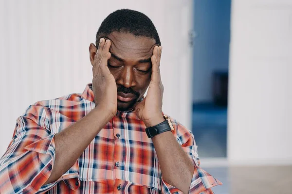 Exhausted upset african american man suffer from headache with his head in his hands. Tired overworked disappointed black guy suffering migraine. Stress at work, burnout, life crisis, failure.