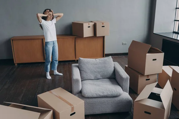 Worried woman holding her head standing near boxes with packed things feels sad due to relocation. Upset girl homeowner or tenant moving out dwelling. Owner eviction, financial problem, foreclosure.