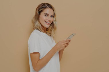 Sosyal ağ hesabının haber kaynaklarını kontrol ederken kameraya bakarak cep telefonu kullanan sevimli kız öğrenci ya da cep telefonuyla internette sörf yapıyor. İnsanlar ve modern teknoloji kavramı