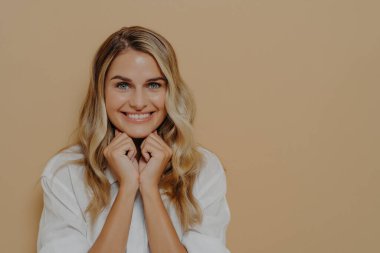 Tatlı, hayalperest genç bir bayanın yakın plan çekimleri, aklında plan yapmak ve gülümsemek keyifli, ellerini çenenin altında kavuşturmak ve kameraya sinsice bakmak, komik ve neşeli bir fikir.