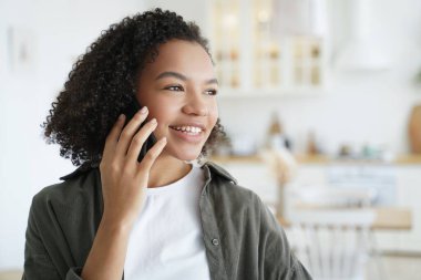 Gülümseyen melez genç kız çağrıya cevap veriyor, telefonla konuşuyor, evde keyifli mobil sohbetler ediyor. Çift ırklı arkadaş canlısı genç bayan iyi haberler aldı, akıllı telefondan sohbet ediyorlar..
