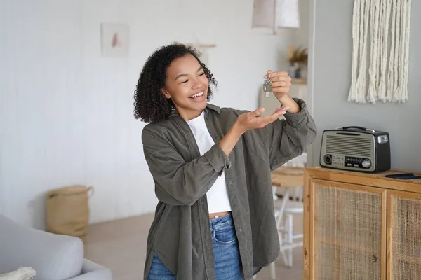 Joyful biracial teen girl tenant homeowner shows home keys to new first house. Happy young lady holding key to apartment, celebrates moving to own housing. Real estate sale, separation from parents.