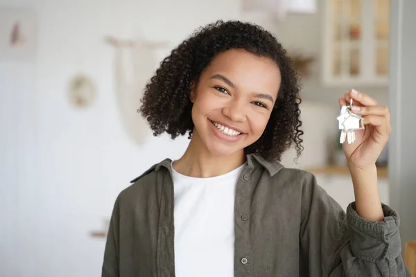 Face of young african american girl which is holding key from new apartment. Carefree teenager is smiling. Happy home owner is relocating. Mortgage loan and real estate purchase conceptual image.